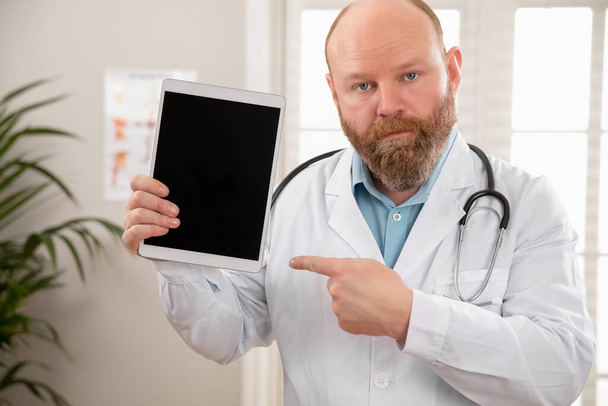 Серьезный взрослый мужчина врач показывает цифровое изображение или отчет на планшете
 - Фото, изображение