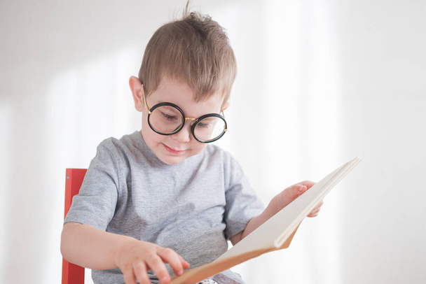Cute toddler boy reading a book in glasses. Smart preschooler. Back to school concept - Fotoğraf, Görsel