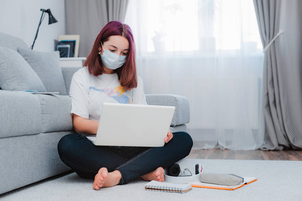 дівчинка-підліток сидить вірус-захисна медична маска з ноутбуком під час онлайн уроку будинку, соціальна дистанція під час карантину, концепція самоізоляції онлайн-освіти домашнього студента коронавірусу
 - Фото, зображення