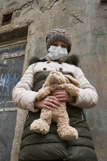 conceito de epidemia e quarentena - uma menina com uma máscara facial e um brinquedo fofinho sozinho na rua da cidade
 - Foto, Imagem