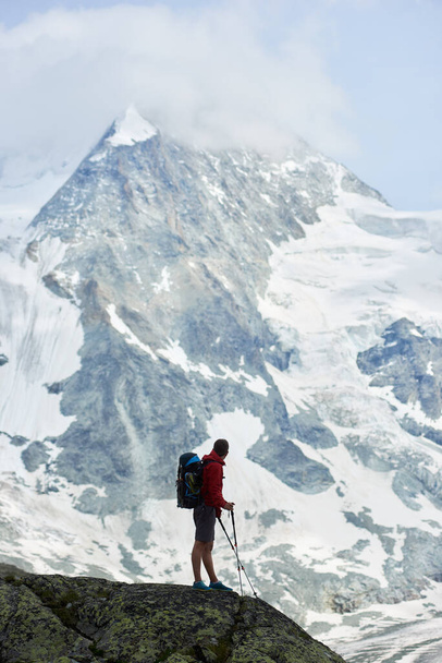 Vertical snapshot of amazing, rocky mount Ober Gabelhorn in snow in the Pennine Alps in Switzerland, located between Zermatt and Zinal, male tourist walking with hiking poles on foreground - Фото, изображение