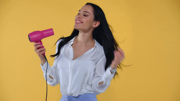 Attractive businesswoman using pink hair blower isolated on yellow - Video, Çekim