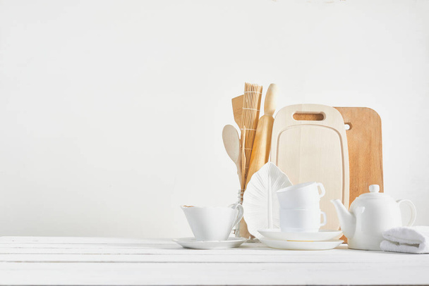 Kitchen background for mockup with spoon, teapot, cups, rolling pin, bowls on wooden table on white background. Blank space for a home kitchen concept. - Photo, Image