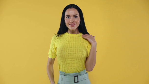 Aantrekkelijk meisje aanraken haar en glimlachen op camera geïsoleerd op geel - Video