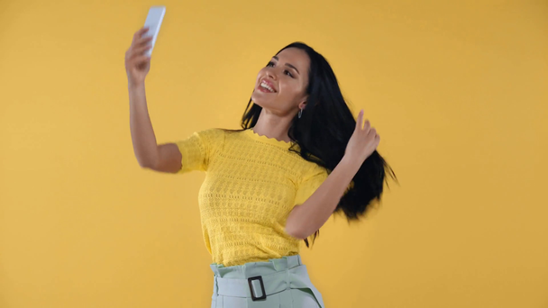 Sarıda izole edilmiş akıllı telefonlu çekici bir kadın selfie çekiyor. - Video, Çekim