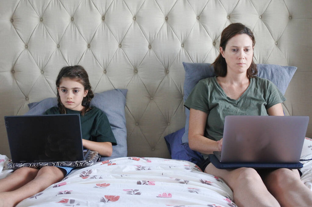Мать и дочь используют лаптограммы в спальне, в то время как вынуждены оставаться дома, потому что правительственные усилия по предотвращению распространения пандемического коронавируса (COVID-19). Настоящие люди. Копирование пространства
. - Фото, изображение