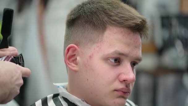 Fryzura młodego człowieka w Barbershop. Zbliżenie mistrza strzyżenia włosów z obcinaczem z tyłu głowy - Materiał filmowy, wideo