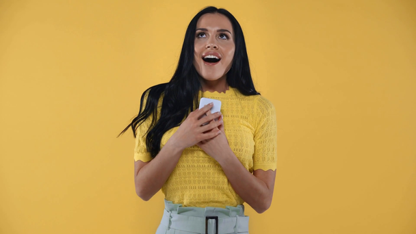 Ενθουσιασμένη κοπέλα με smartphone που δείχνει ναι χειρονομία στην κάμερα απομονωμένη στο κίτρινο - Πλάνα, βίντεο
