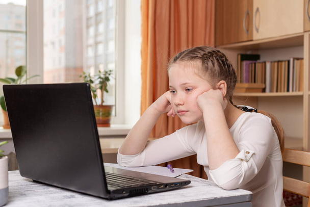 Serious schoolgirl looks at a laptop screen. Distance learning online education, home school, home education, quarantine concept - Image - Φωτογραφία, εικόνα