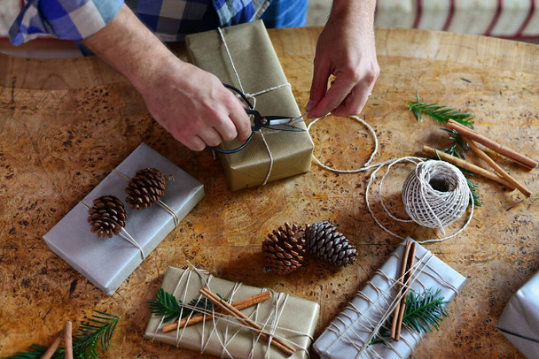 Jovem hipster embrulhando seus presentes de Natal modernos e chiques na mesa de madeira
 - Foto, Imagem