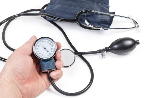 Aneroid manometer of the manual sphygmomanometer in men's hand against the rest of the same device and stethoscope on a white background close-up in selective focus - Photo, Image