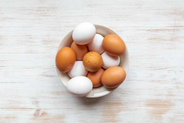 Organická vejce ve volném výběhu v misce. Talíř s hnědými a bílými slepičími vejci na dřevěném stole. Detailní záběr hnědé a bílé vejce v misce na dřevěném pozadí. Pohled shora, plochý. Přírodní zdravá výživa koncept - Fotografie, Obrázek