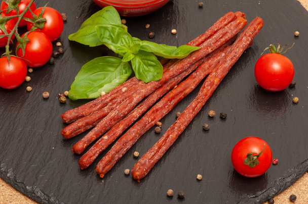 thin long sausage with sauce, cherry tomatoes and basil on a black graphite board - Fotografie, Obrázek