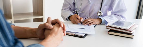 Пацієнт уважно слухає лікаря-чоловіка, який пояснює симптоми пацієнта або задає питання, коли вони обговорюють документи разом на консультації
 - Фото, зображення
