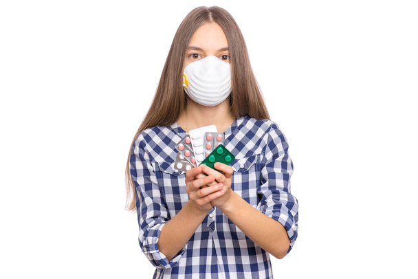 Concept of coronavirus quarantine. COVID-19 - home isolation. Child wearing medical protective face mask to health protection from influenza virus, isolated on white background. Teen girl holds pills. - Фото, изображение