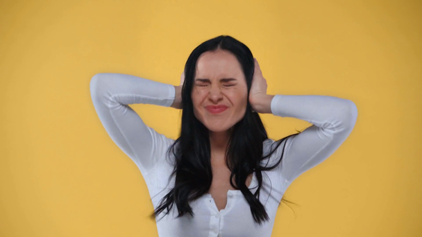 Θυμωμένη γυναίκα που καλύπτει αυτιά και ουρλιάζει απομονωμένη στο κίτρινο - Πλάνα, βίντεο
