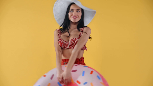 Cheerful girl in sun hat holding swim ring isolated on yellow - Metraje, vídeo