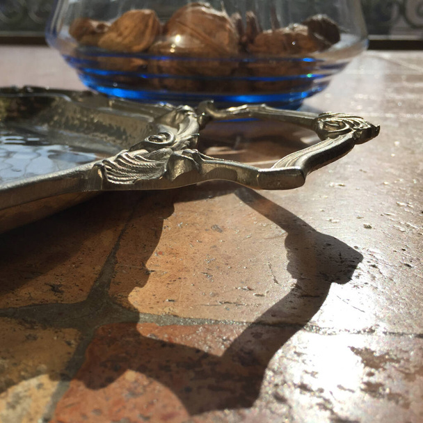 Detalhe do punho de uma bandeja antiga. No fundo um top em tartarugas italianas e algumas nozes em uma tigela de vidro
 - Foto, Imagem