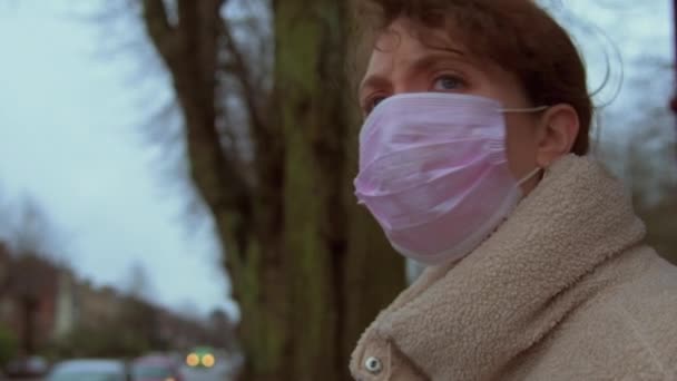Mulher caucasiana vestindo uma máscara facial espera em uma parada de ônibus
 - Filmagem, Vídeo