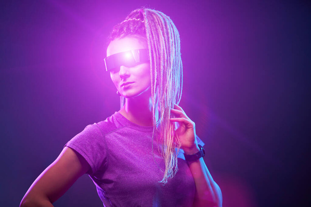 Fiatal lány napszemüvegben nézi a kamerát neon fényben - Fotó, kép