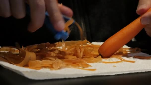 Πρόσωπο που ξεφλουδίζει το καρότο πορτοκαλιού με τους αποφλοιωτές λαχανικών στο ξύλο κοπής στο σπίτι - Πλάνα, βίντεο