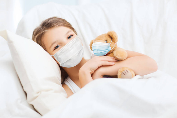 girl wearing medical mask with teddy bear in bed - Фото, зображення
