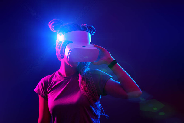 La mujer está usando auriculares de realidad virtual. Retrato de estudio de luz de neón. - Foto, imagen