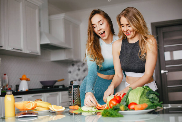 Two sports girl in a kitchen with vegetables - Fotó, kép