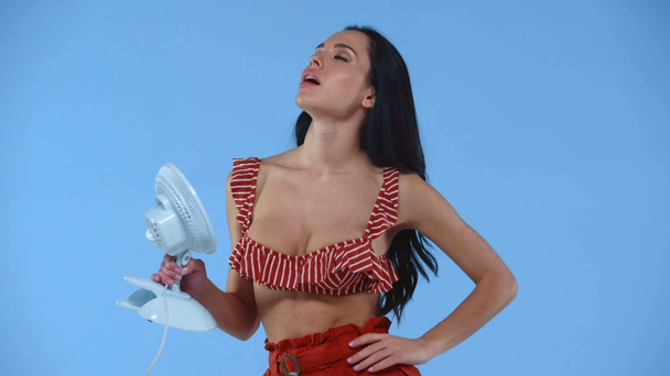 Sexy fille en soutien-gorge de maillot de bain en utilisant un ventilateur électrique isolé sur bleu
  - Séquence, vidéo