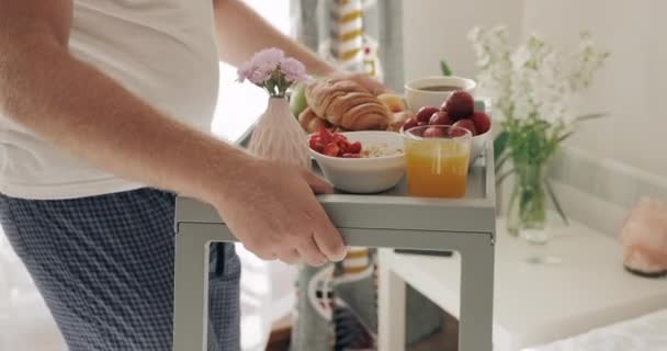 Loving man serving breakfast in bed for his girlfriend and sitting near her. Smiling woman waiting for her boyfriend holding tray with food and giving him kiss. Concept of family. - Filmati, video