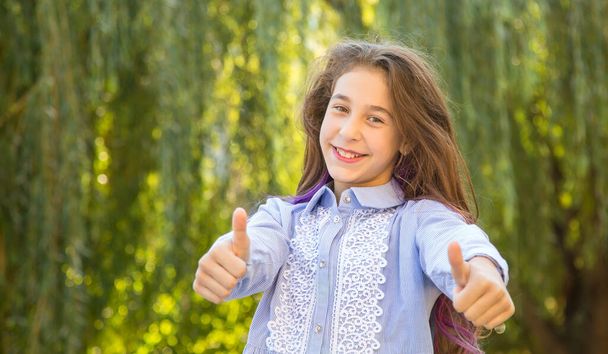 Excellent! Beautiful teenage girls showing thumbs up, standing on the background of a sunny day in the park. - Фото, изображение