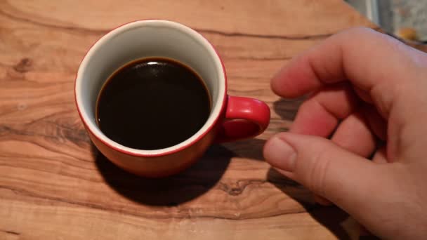 Close up shot of a red coffee cup on the outside and white on the inside resting on a wooden cutting board. The hand of a Caucasian man grabs it by the handle and lifts it, then it is put down. - Footage, Video