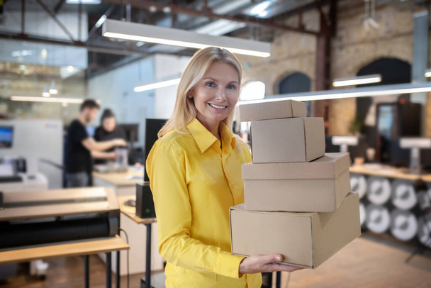 Blonde Frau hält Stapel von Kisten und lächelt - Foto, Bild