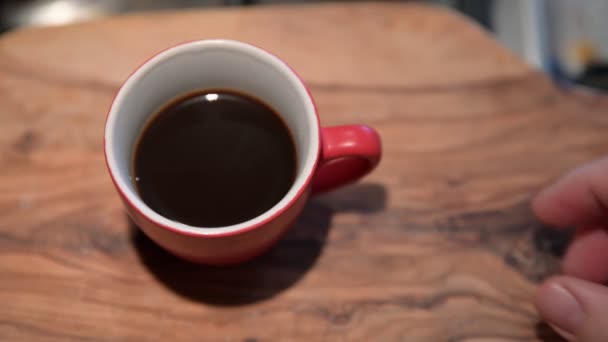 Close-up image of a red coffee cup on the outside and white on the inside resting on a wooden cutting board. A Caucasian man's hand grabs her by the handle and lifts her away. - Záběry, video