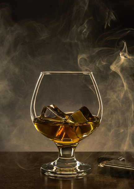 木製のテーブルの上にアルコールとアイスキューブとガラス。背景の煙とコピースペース. - 写真・画像