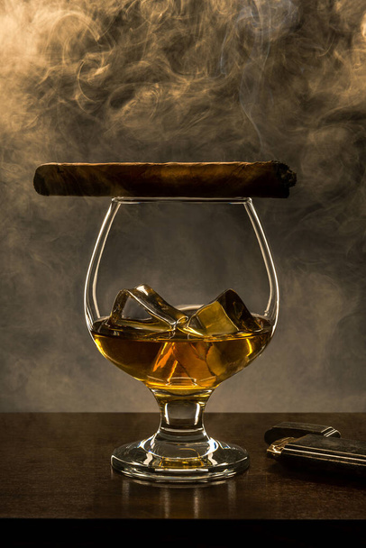 Smoking Cuban Cigar on Top of Elegant Whisky Glass with Ice Cubes. Copy Space Background. - Photo, Image