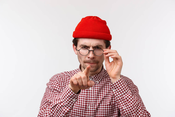 Portrait en gros plan d'un jeune homme adulte sérieux et drôle en bonnet rouge, portant des lunettes pour lire quelque chose, aveugle sans lunettes, pointant la caméra comme choisissant le produit, plissant ont troublé la vue
 - Photo, image