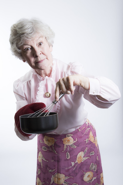 idős nő egy edénybe, és habverővel holding - Fotó, kép