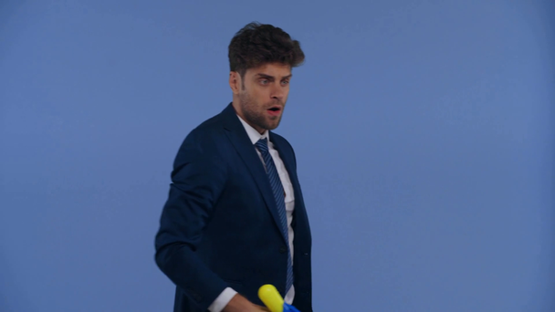 Handsome businessman playing with toy gun isolated on blue - Footage, Video