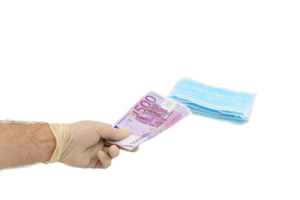 One hand in white protective gloves buys a pack of blue medical masks for money with 500 Euro banknotes. Concept of buying a mask in Europe, protection against the virus. Shortage of medical masks, high cost. Isolated white background. - Foto, Bild