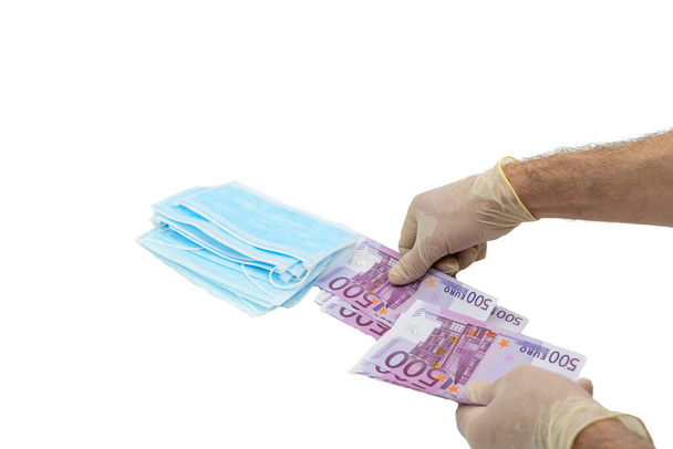 Two hands in white protective gloves buy a pack of blue medical masks for money with 500 Euro banknotes. Concept of buying a mask in Europe, protection against the virus. Shortage of medical masks, high cost. Isolated white background. - Foto, afbeelding
