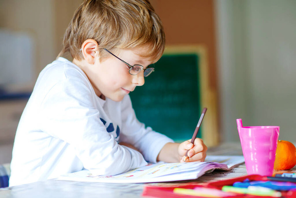 Hard-working happy school kid boy making homework during quarantine time from corona pandemic disease. Healthy child writing with pen, staying at home. Homeschooling concept - Foto, Bild