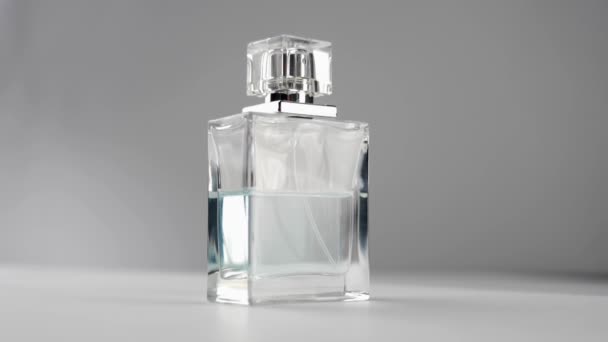 シアン香水やエッセンシャルオイルとフラット浮上ボトルはゆっくりと灰色の背景に白いテーブルの上に回転します。香りと香りの概念。閉めろ。スローモーション - 映像、動画