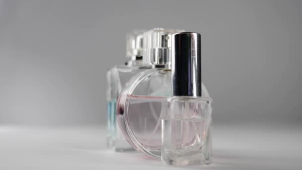 Three bottles with pink, cyan and transparent perfumes or essential oils slowly rotates on the white table against grey background. Concept of aroma and smell. Close up. Slow motion - Footage, Video