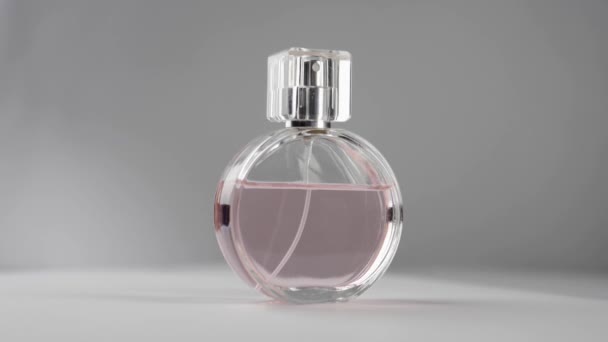 Oval surfaced bottle with pink perfumes or essential oils slowly rotates on the white table against grey background. Concept of aroma and smell. Close up. Slow motion - Footage, Video