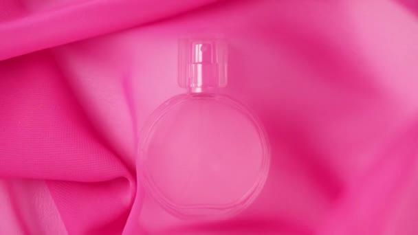Ovale fles met roze parfums of etherische oliën staat op de witte tafel onder een roze stof. Roze stofgolven, fladderen abrupt weg van de tafel en leggen parfums bloot. Sluit maar af. Langzame beweging - Video