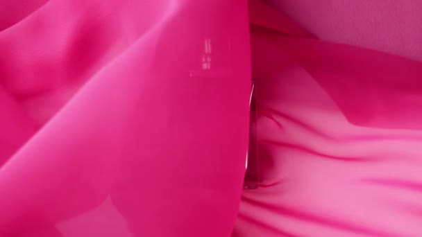 Vlakke fles met cyaan parfums of etherische oliën zit op de roze doek. Roze stof fladdert rond en zwaait rond de fles. Concept van aroma en geur. Sluit maar af. Langzame beweging - Video