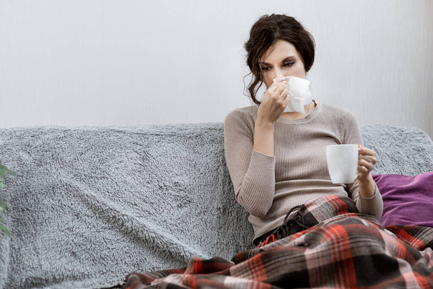 Sick woman suspected of covid-19, being at home in bed, measures the temperature and sneezes. Sick woman sitting under the blanket. Girl is quarantined with suspected coronavirus - Foto, Imagen