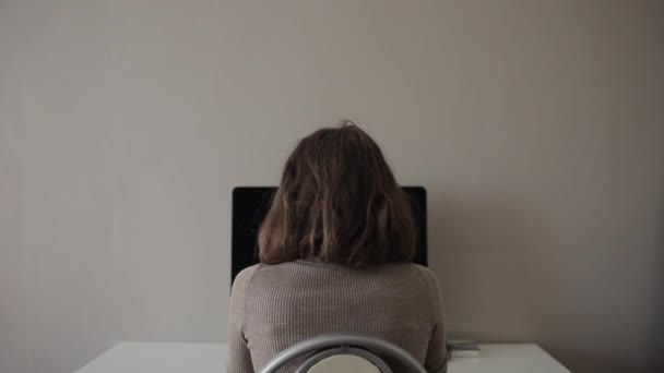 Πίσω όψη ενός κοριτσιού που κάθεται σε ένα τραπέζι και δουλεύει σε έναν υπολογιστή. Κοντινό πλάνο - Πλάνα, βίντεο