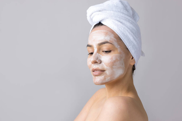 Schoonheidsportret van vrouw in witte handdoek op het hoofd brengt crème aan op het gezicht. Huidverzorging eco biologische cosmetische spa ontspannen concept. - Foto, afbeelding